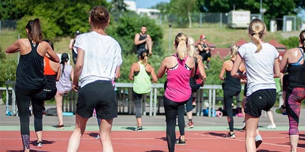 A male and female instructor lead an outdoor aerobic exercise course for a group of women.